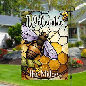 May include: A welcome garden flag with a bee and honeycomb design. The flag is yellow, brown, and purple with the text "Welcome the Millers".