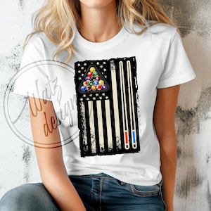 May include: White t-shirt with a black and white American flag design featuring a pool ball rack and two pool cues. The flag has a distressed look.