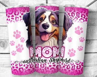 Op de afbeelding: Een roze en witte tumbler met een cartoon Australian Shepherd-hond met het woord "MOM" en de tekst "Australian Shepherd" onderaan. De tumbler heeft een roze glitterontwerp.