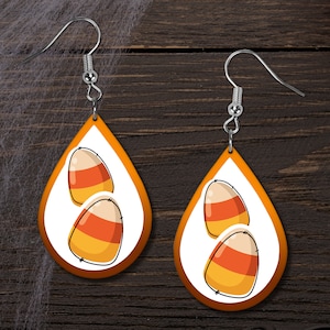 May include: A pair of orange teardrop-shaped earrings with a white background and a design of two candy corn pieces.