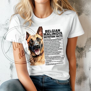 May include: White t-shirt with a graphic of a Belgian Malinois dog and a nutrition facts label that reads "Belgian Malinois Nutrition Facts. Serving Size: 1 cup of love." The label lists various traits of the breed, such as loyalty, intelligence, courage, and sensitivity.