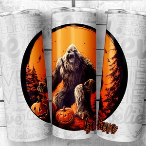 May include: A white tumbler with a design of a Bigfoot holding a pumpkin in a forest setting with an orange and red sunset in the background. The tumbler has the word "believe" printed on it.