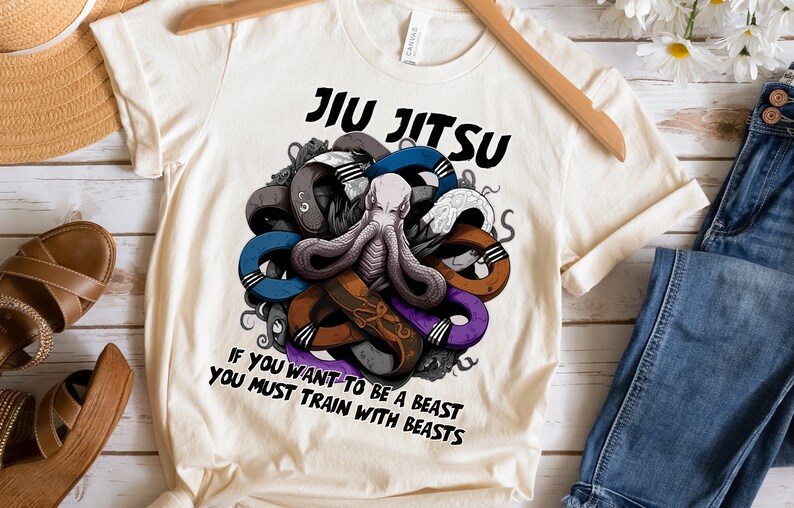 May include: A white t-shirt with a graphic of an octopus surrounded by colorful belts. The text "JIU JITSU" is above the octopus and the text "IF YOU WANT TO BE A BEAST YOU MUST TRAIN WITH BEASTS" is below the octopus.