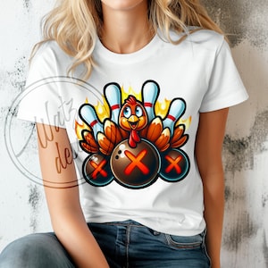 Pode incluir: Uma camiseta branca com um desenho animado de um peru usando um chapéu de boliche e segurando pinos de boliche. O peru está cercado por bolas de boliche com um 'X' nelas.