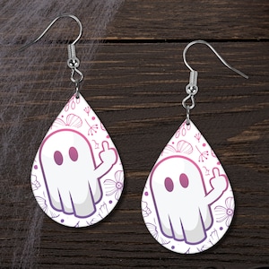 May include: A pair of dangle earrings featuring a white ghost with a middle finger up, surrounded by pink and white floral designs on a white background.