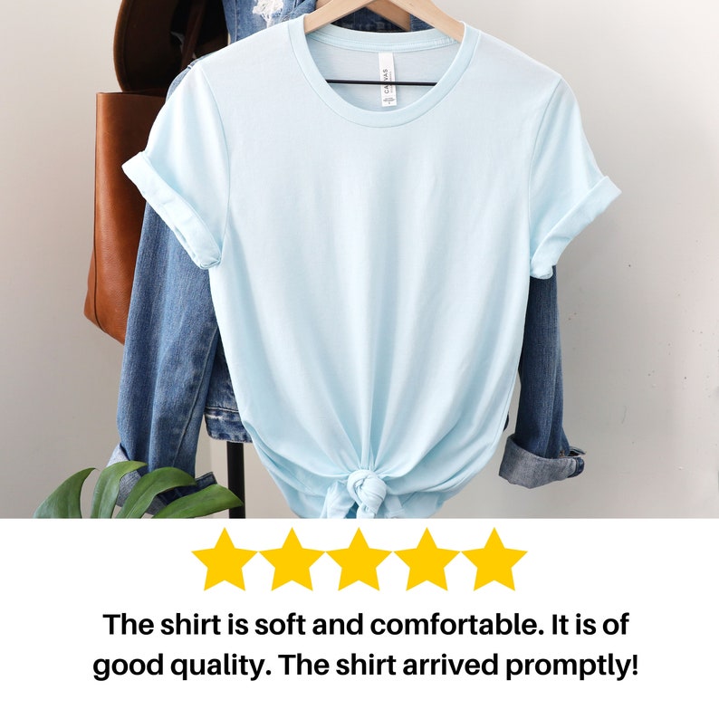 Puede incluir: Una camiseta azul claro con las mangas remangadas. La camiseta est&aacute; anudada en la parte inferior.