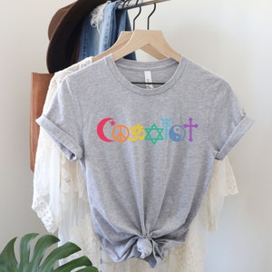Puede incluir: Camiseta gris con un dise&ntilde;o arco&iacute;ris que presenta s&iacute;mbolos religiosos y la palabra "Coexist".