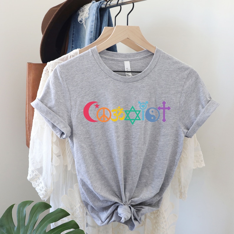 Puede incluir: Camiseta gris con un dise&ntilde;o arco&iacute;ris que presenta s&iacute;mbolos religiosos y la palabra "Coexist".