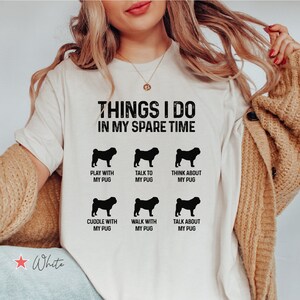 Może przedstawiać: Biała koszulka z tekstem "Things I do in my spare time" i sześcioma czarnymi sylwetkami mopsów z tekstem opisującym czynności, takie jak "Play with my pug" i "Talk about my pug".