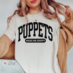 May include: White t-shirt with black text that reads "Puppets Make Me Happy".