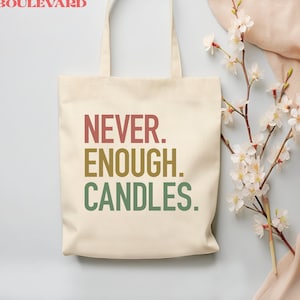 May include: A white canvas tote bag with the text "NEVER. ENOUGH. CANDLES." printed in red, orange, yellow, and green. The bag is sitting on a light blue surface with a branch of white blossoms.
