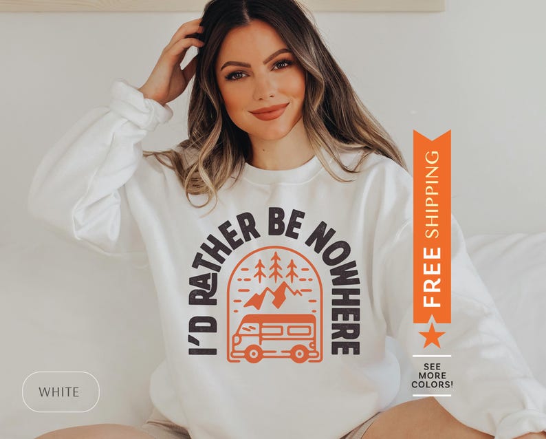 Pode incluir: Camisola branca com um gr&aacute;fico de uma autocaravana em frente a uma cordilheira com &aacute;rvores. O texto "I'd Rather Be Nowhere" est&aacute; em um semic&iacute;rculo em torno da autocaravana.