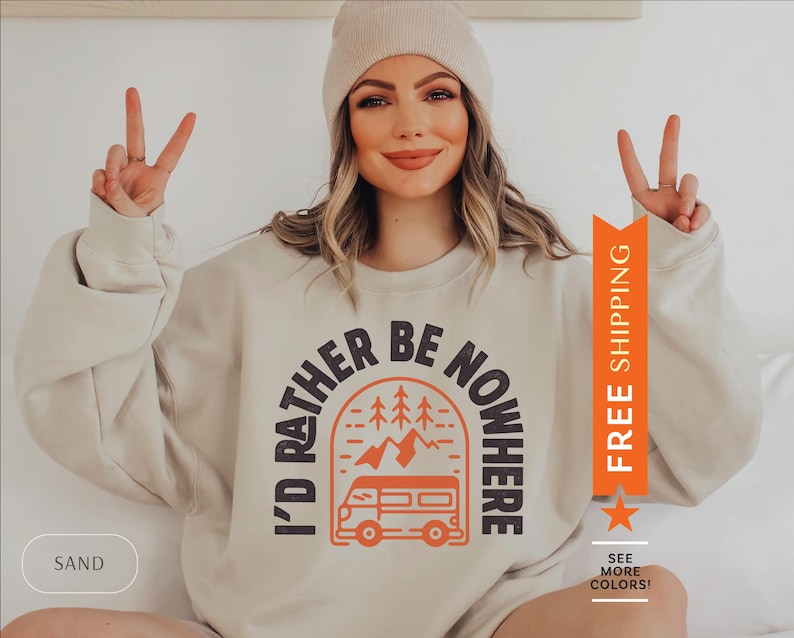 Pode incluir: Uma camisa de moletom bege com o texto "I'd rather be nowhere" em um arco preto com uma van e pinheiros dentro. O texto est&aacute; em laranja e preto.