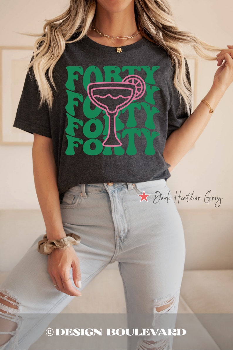 May include: A dark heather grey short-sleeve t-shirt featuring a pink outline of a margarita glass with a lime slice. The word FORTY is printed in a repeating green wavy font pattern behind the glass. The shirt has a crew neckline and short sleeves.