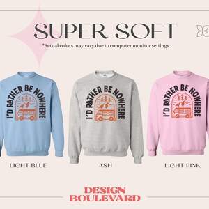 Pode incluir: Tr&ecirc;s sweatshirts de gola redonda em azul claro, cinza claro e rosa claro com o texto "I'd rather be nowhere" em preto com um gr&aacute;fico de uma autocaravana e montanhas em laranja. O texto "Super Soft" est&aacute; no topo da imagem.