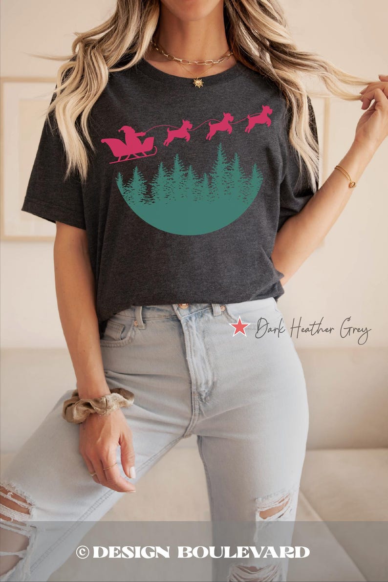 May include: Dark heather grey t-shirt featuring a pink Santa Claus in a sleigh pulled by three pink dogs over a green forest design. The text "Dark Heather Grey" is printed on the shirt. The brand name "DESIGN BOULEVARD" is printed at the bottom.