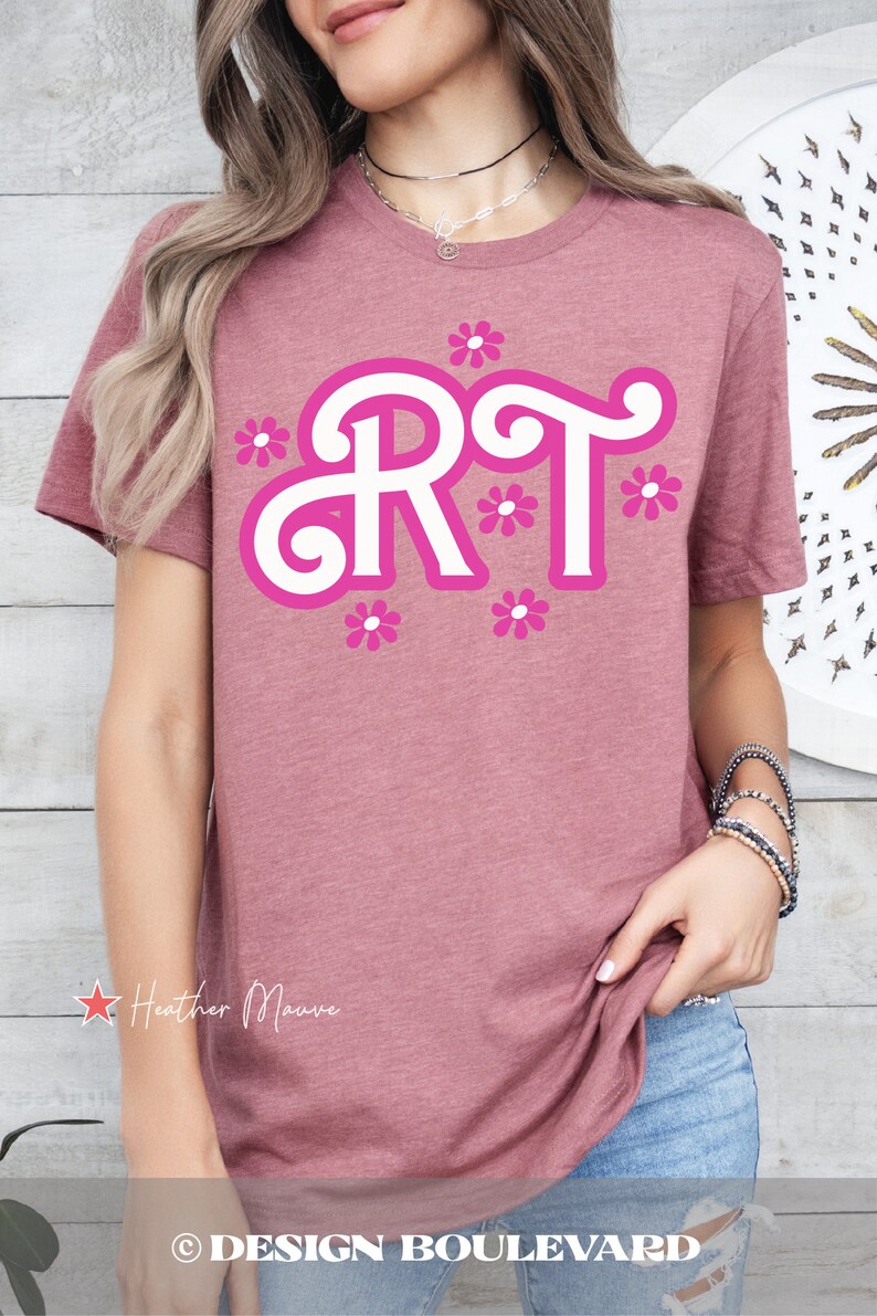 Pu&ograve; includere: Una t-shirt color malva brughiera con una grafica bianca delle lettere "RT" in un font stilizzato con contorni rosa e fiori rosa intorno alle lettere. Il testo "Heather Mauve" &egrave; visibile nell'angolo in basso a sinistra dell'immagine.