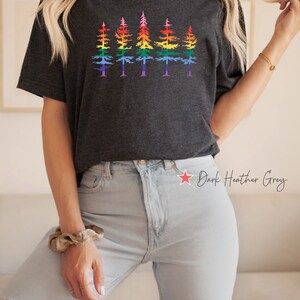 Op de afbeelding: Een donkergrijs gem&ecirc;leerd T-shirt met korte mouwen en een grafische print van vijf dennenbomen op een rij. Elke boom is voorzien van horizontale strepen in een regenboogkleurverloop. Het T-shirt heeft een ronde hals en een relaxte pasvorm.