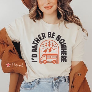 May include: A white t-shirt with a black graphic that says "I'd rather be nowhere" with a mountain and a van design in orange.