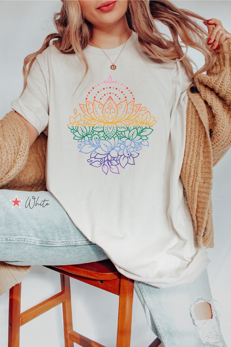 K&ouml;nnte beinhalten: Ein wei&szlig;es T-Shirt mit einem regenbogenfarbenen Lotusbl&uuml;ten-Design. Das Design zeigt ein mandalaartiges Muster mit filigranen Details. Das Shirt wird von einer Person mit langen blonden Haaren getragen.