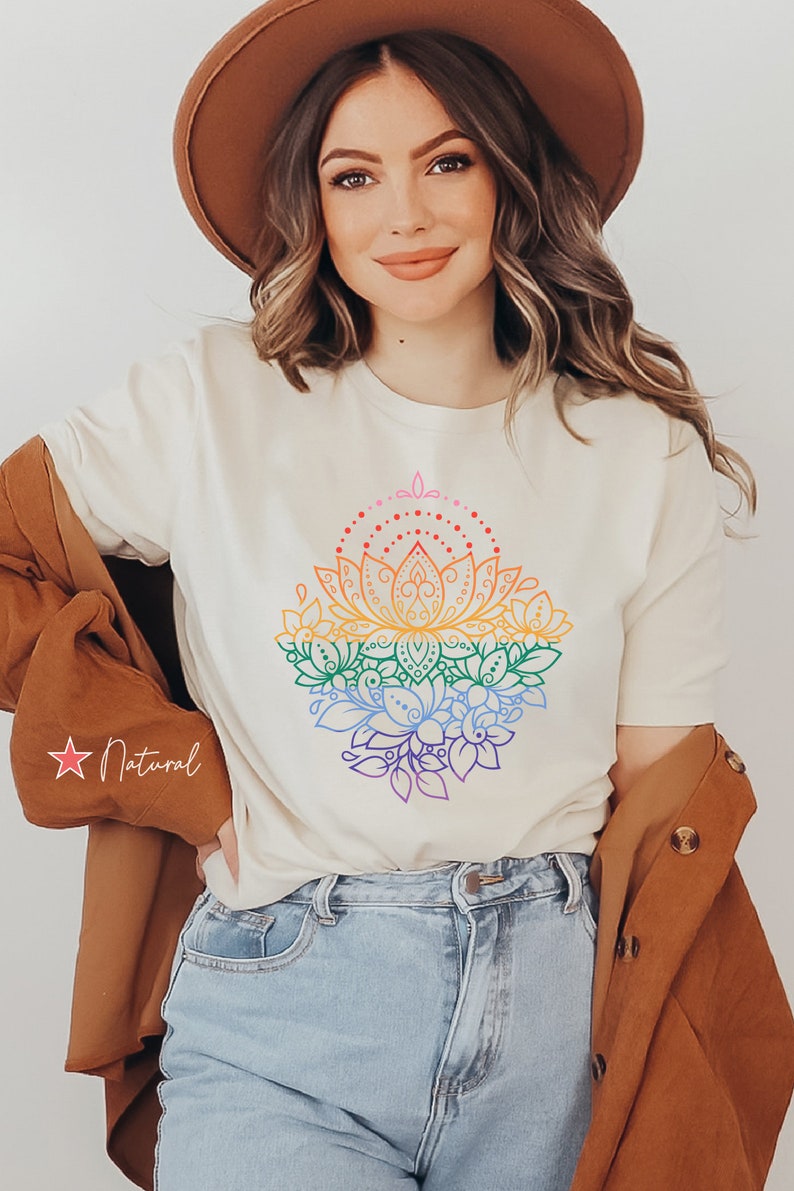 K&ouml;nnte beinhalten: Ein wei&szlig;es T-Shirt mit einem Regenbogen-Mandala-Design, das eine Lotusblume und florale Akzente zeigt. Das Design ist in einem Regenbogen-Farbschema umrandet.