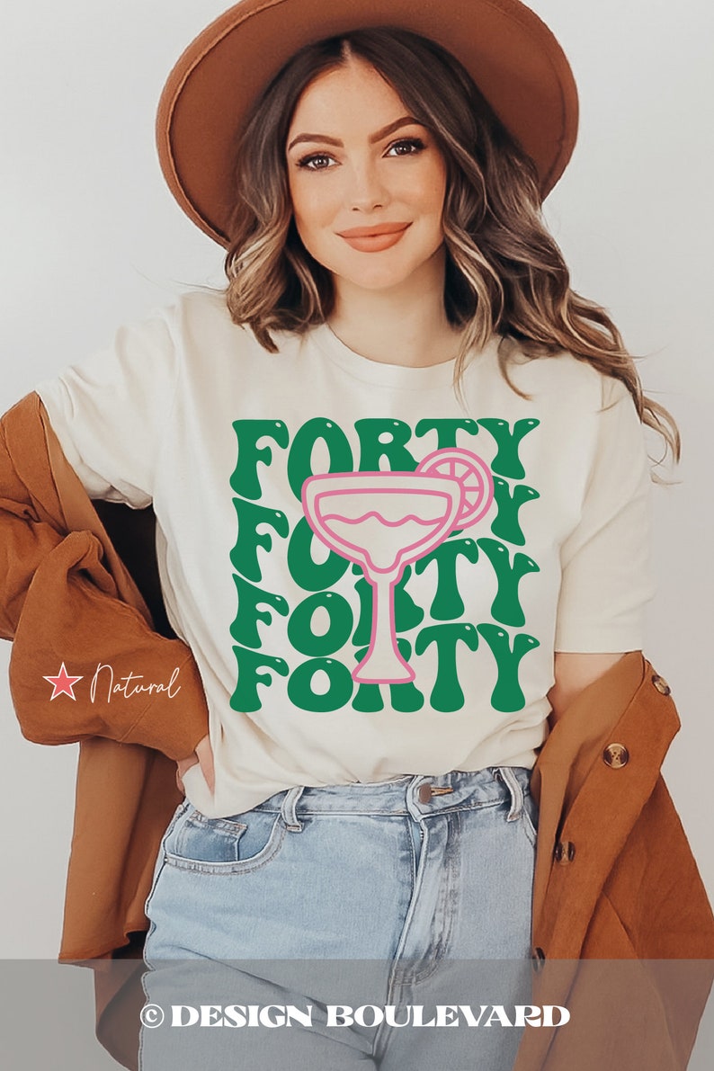May include: A cream-colored short-sleeve t-shirt featuring a large graphic print of a pink margarita glass centered among the word FORTY repeated four times in a bold, wavy green font. The shirt is worn with a brown hat and a brown jacket.