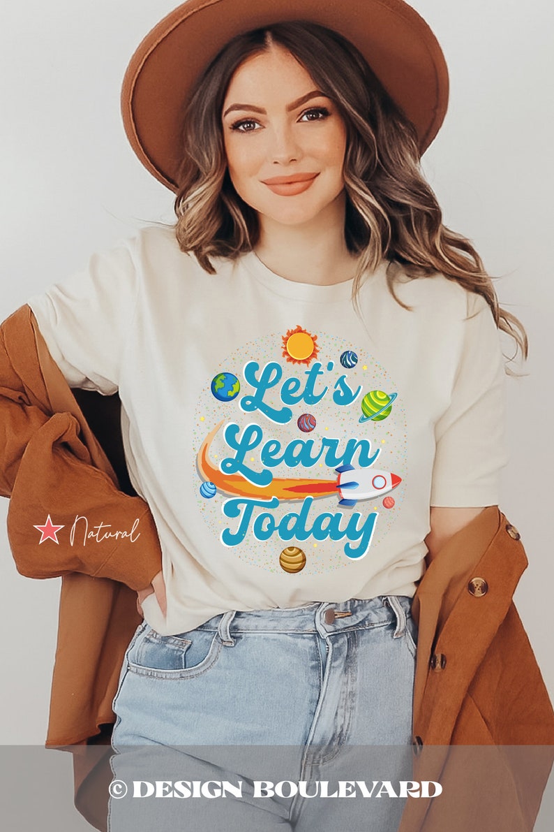 Pode incluir: Uma camiseta branca com um gr&aacute;fico azul e laranja que diz "Let's Learn Today" com planetas e um foguete. A camiseta est&aacute; em uma modelo que usa um chap&eacute;u marrom e jeans azul.