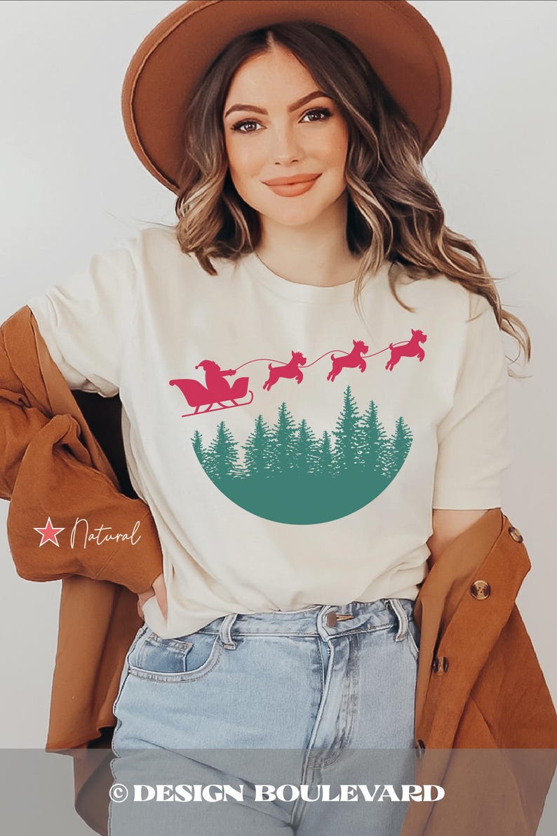 May include: Cream-colored t-shirt featuring a festive design of Santa Claus in a sleigh pulled by reindeer over a forest silhouette. The shirt has a round neck and short sleeves. The text "DESIGN BOULEVARD" is at the bottom.