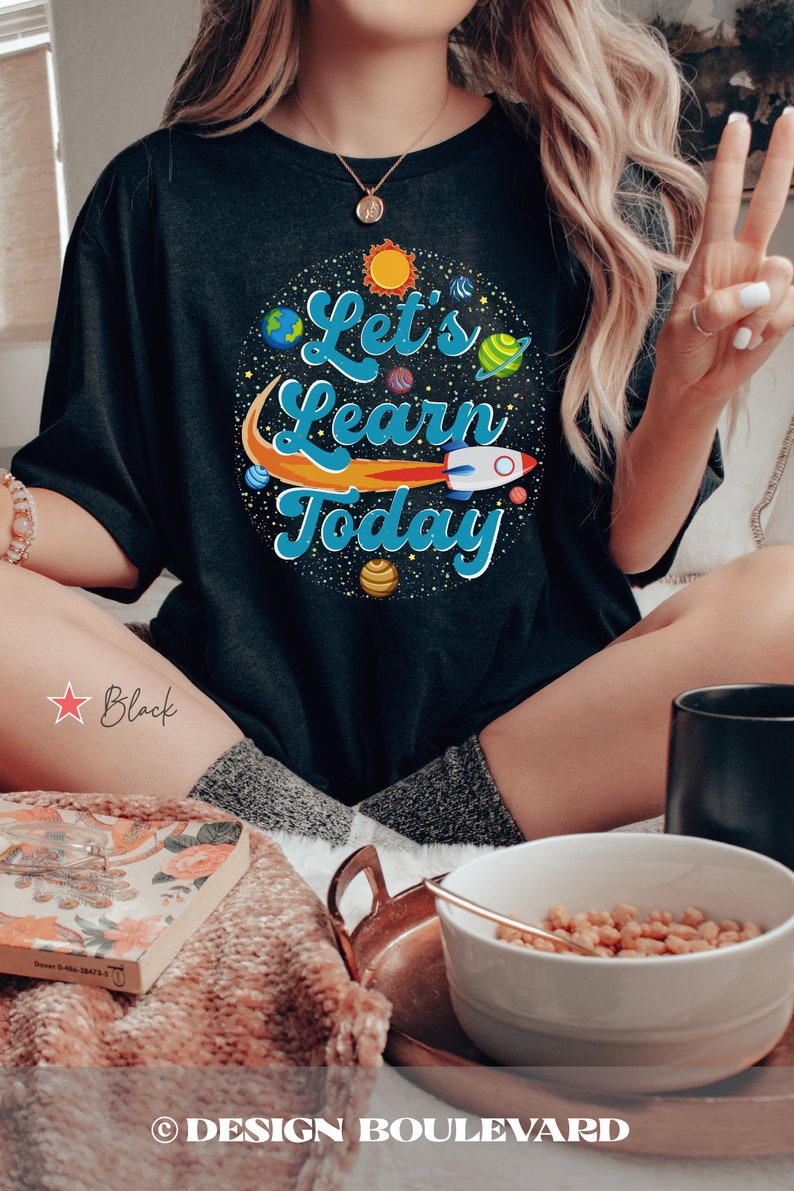 Pode incluir: Camiseta preta com um gr&aacute;fico de planetas, um foguete e o texto "Let's Learn Today".