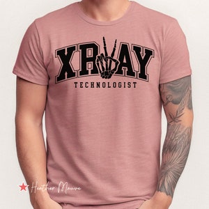 May include: A heather mauve t-shirt featuring a black graphic of a skeleton hand making a peace sign. The text "X-RAY TECHNOLOGIST" is printed below the graphic.