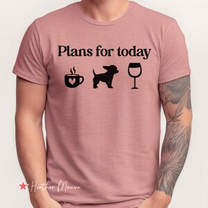 May include: A heather mauve short-sleeve t-shirt featuring the black text "Plans for today" above three black icons: a coffee mug with a heart, a silhouette of a small dog, and a wine glass. The shirt has a crew neckline and a standard fit.