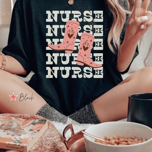 May include: Black t-shirt with the word "NURSE" repeated five times in a distressed font. The word "NURSE" is layered with a pair of pink cowboy boots with flames and hearts on them.