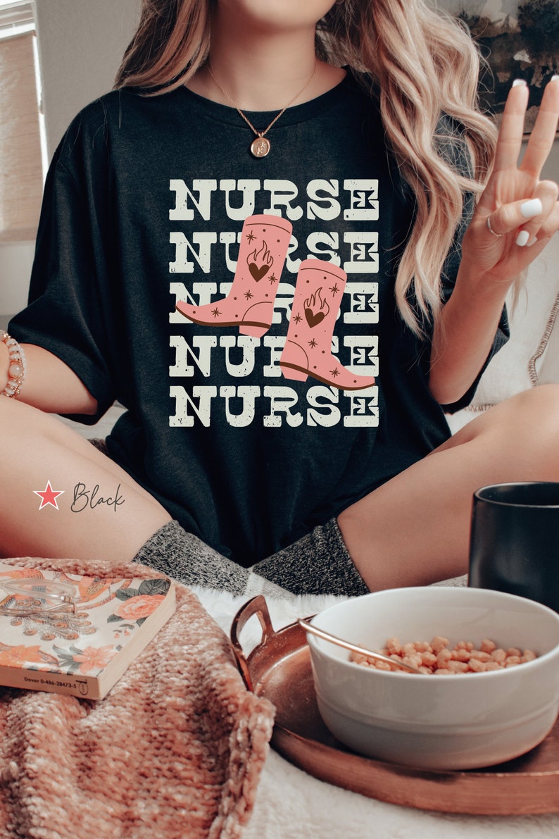May include: Black t-shirt with the word "NURSE" repeated five times in a distressed font. The word "NURSE" is layered with a pair of pink cowboy boots with flames and hearts on them.