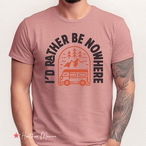 May include: A heather mauve t-shirt with a graphic print of a camper van driving through a mountain landscape with trees. The text "I'd rather be nowhere" is printed in a black semi-circle around the graphic.
