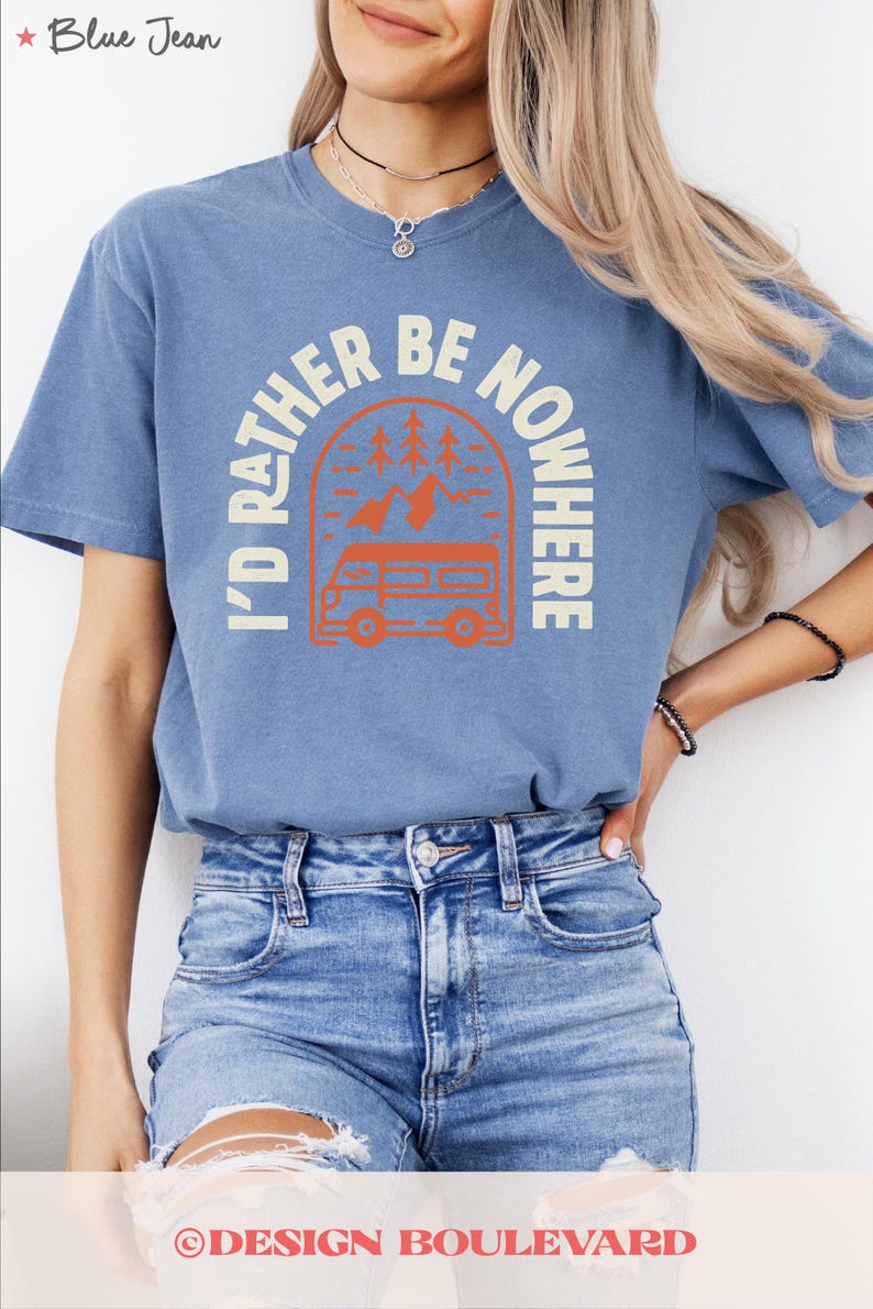 May include: A blue short-sleeved t-shirt with the cream text "I'D RATHER BE NOWHERE". The graphic shows an orange camper van, trees, and mountains. The shirt is worn with blue denim jeans.