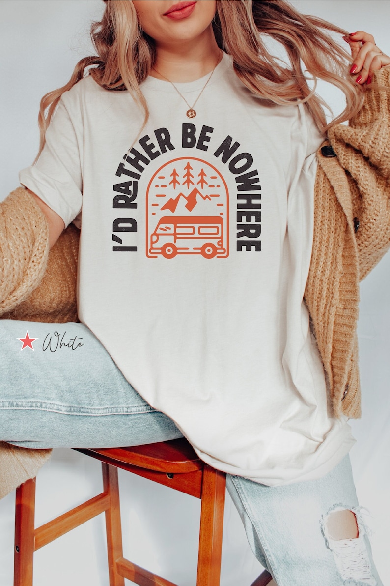 May include: A white t-shirt with the text "I'd rather be nowhere" in a black arch with a red camper van and mountains inside. The text is in a black font and the camper van is red.