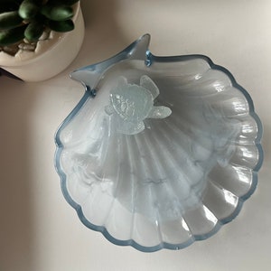 May include: A light blue glass seashell dish with a white swirl design and a small, clear turtle figurine in the center.