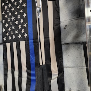 May include: A black, white, and blue American flag with a blue stripe, hanging near a weightlifting cable with black handles. The flag features white stars on a black background and white and black stripes.