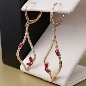 Può includere: Orecchini pendenti in oro rosa con un design a goccia tempestato di diamanti e tre accenti di rubino.