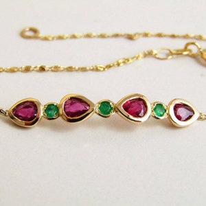 May include: A gold bracelet with alternating teardrop-shaped red gemstones and small round green gemstones. The bracelet has a fine chain and a secure clasp, showcasing a classic jewellery design.