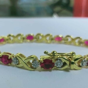 Puede incluir: Un brazalete de oro con un diseño delicado que presenta piedras de rubí rojo y diamantes transparentes alternados.