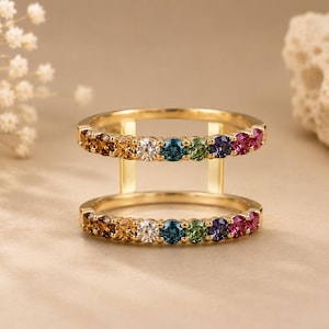Peut inclure: Une bague double en or composée de deux rangées parallèles de pierres précieuses rondes aux couleurs de l'arc-en-ciel, incluant des tons ambre, blanc, bleu, vert, violet et rose, reliées par deux barres verticales en or de chaque côté.