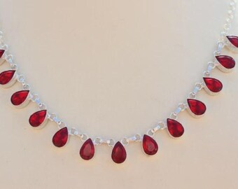 Puede incluir: Un collar de plata con un colgante de piedra preciosa roja en forma de lágrima. El collar tiene una cadena delicada y presenta varias piedras preciosas rojas.