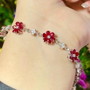 May include: A silver bracelet with red ruby and clear diamond flower accents.
