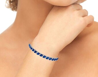 May include: A silver tennis bracelet with blue marquise-shaped gemstones.
