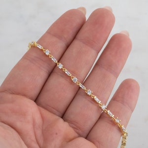 May include: A gold chain bracelet with alternating round and baguette-shaped clear cubic zirconia stones.