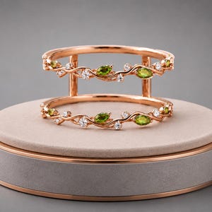 May include: A rose gold double-band ring featuring a vine-inspired design. The two bands are connected by vertical bars and are adorned with marquise-cut green peridot gemstones and small round clear white diamonds set along the metal branches.