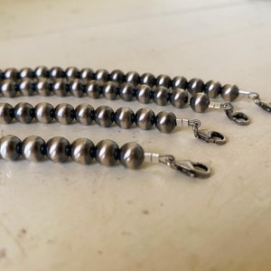 May include: Three strands of silver beads with a clasp on each end. The beads are round and have a dark, oxidized finish.