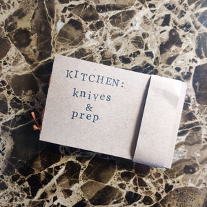 May include: A brown paper booklet with the text "KITCHEN: knives & prep" printed in black.