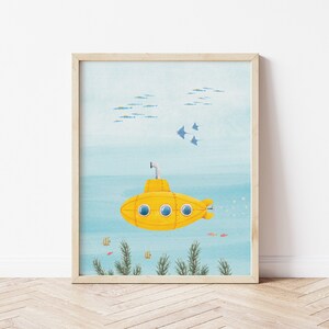 Op de afbeelding: Een ingelijste kunstdruk met een gele onderzeeër in een onderwaterlandschap. De illustratie bevat vissen, zeegroei en roggen, tegen een blauwe en lichtblauwe achtergrond. De print zit in een houten lijst.
